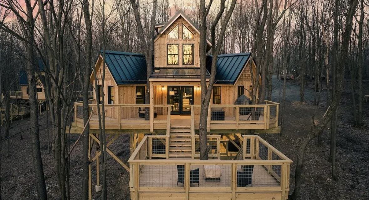 A rentable glamping treehouse at dusk, windows lit above stacked decks