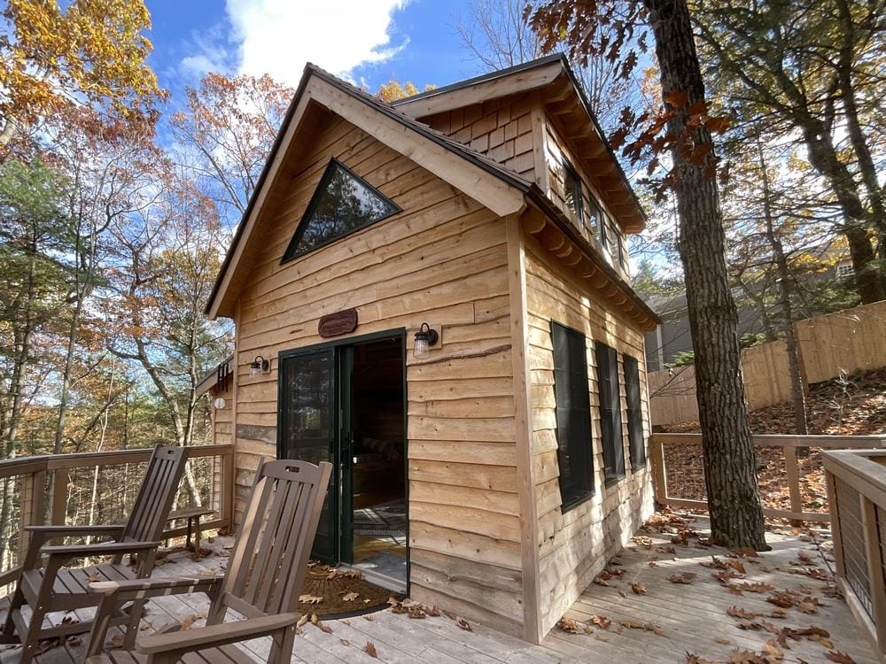 A cedar-clad build with a deck and rocking chairs in autumn woods